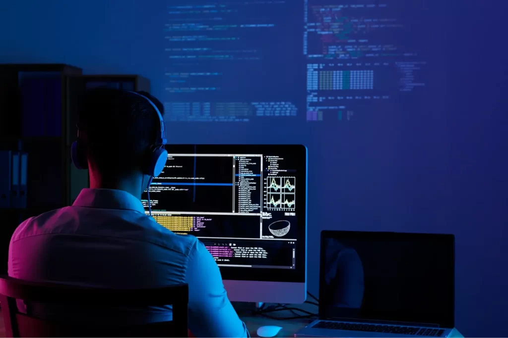 Node.js developer coding backend application and analyzing server data on multiple monitors at workstation
